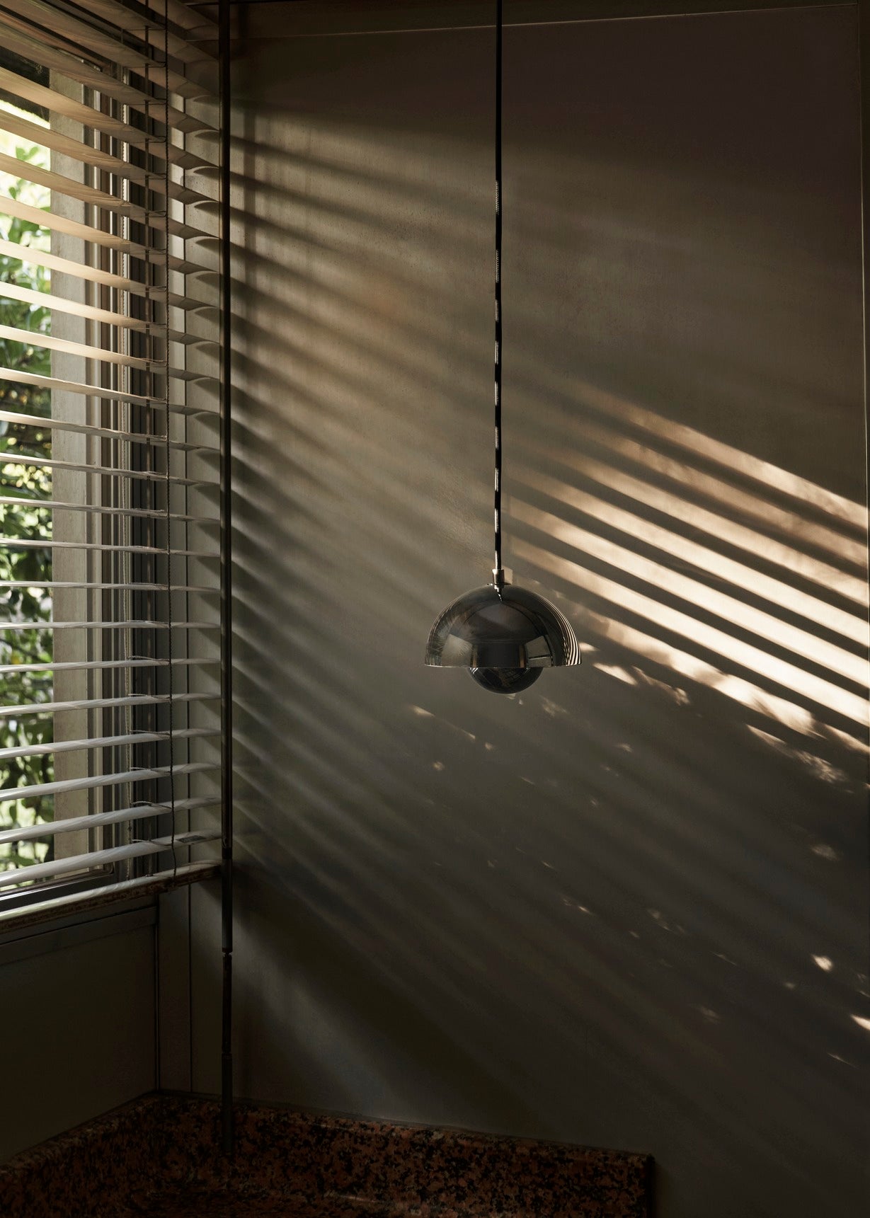 A dark-colored, Flowerpot VP10 pendant lamp hangs from a cord, casting a soft glow. Sunlight streams through blinds on the left.